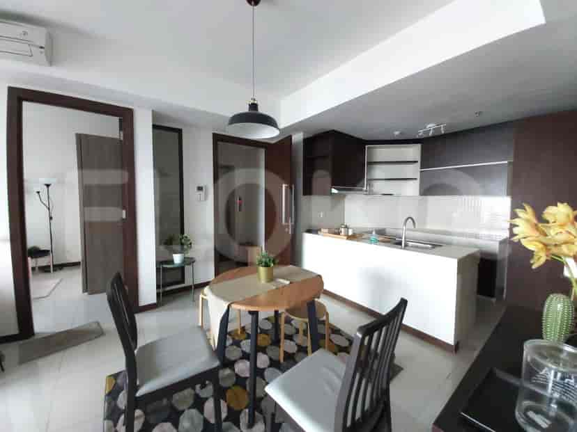 Dapur terbuka dengan meja dapur putih dan lemari kayu gelap, bersebelahan dengan area makan dengan meja bundar.