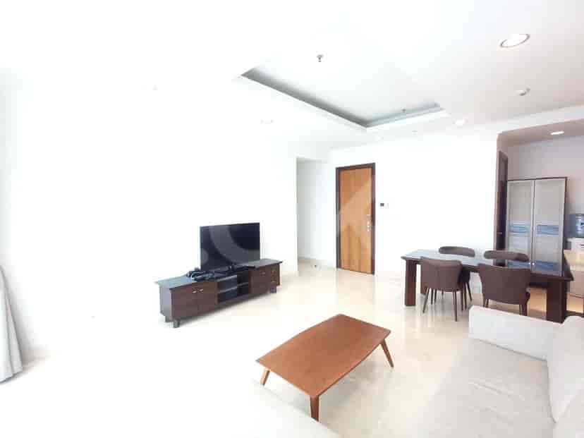 A living room with a TV console, a low coffee table, and a dining set. The room has white walls and a dropped ceiling.