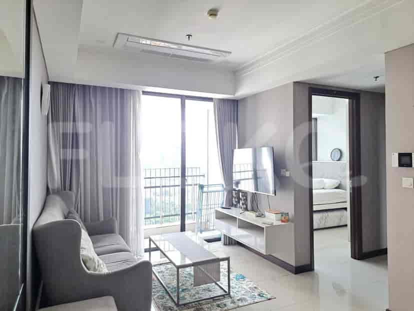 A modern living room with a grey sofa, a glass coffee table, a wall-mounted TV, and large windows with sheer curtains.