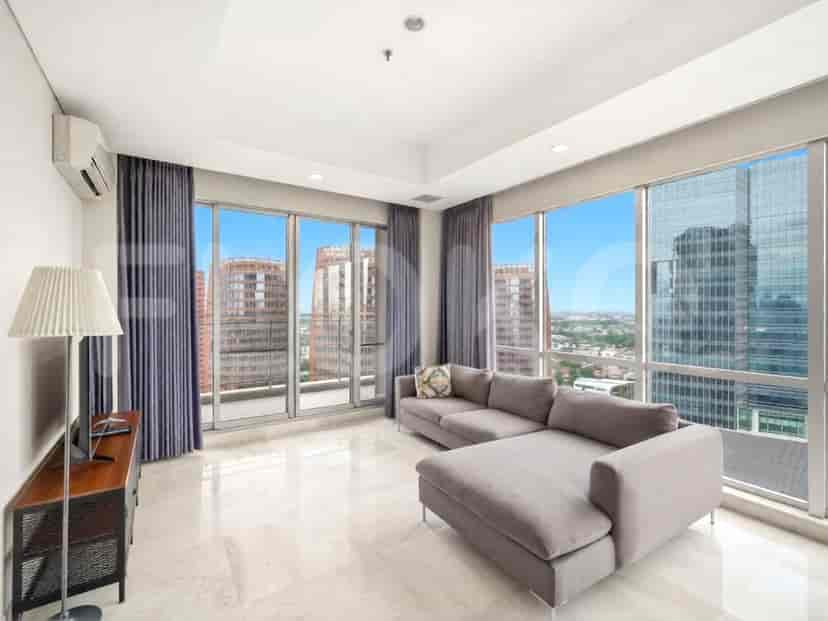 A spacious living room with an L-shaped grey sofa, a floor lamp, and large windows offering a city view.