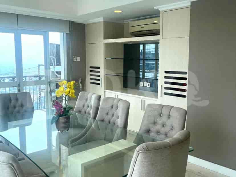 A dining room featuring a glass-top dining table with upholstered chairs and a built-in cabinet with shelving.