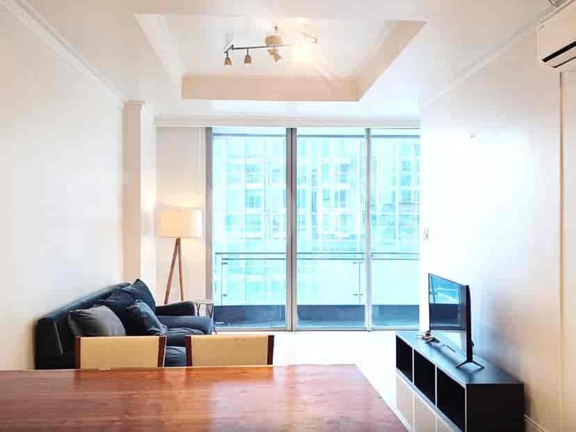 A modern living room with a dark sofa, chairs, a wooden dining table, and large windows offering a city view.