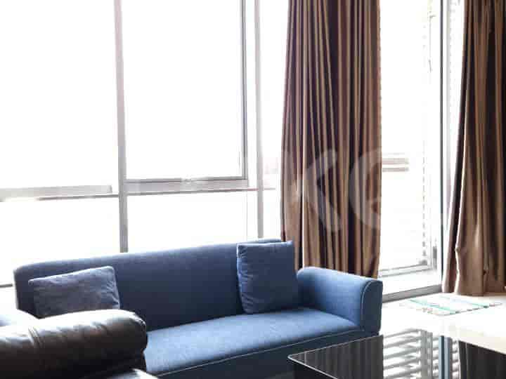 A modern living room with a blue sofa, dark coffee table, and large windows with brown curtains.