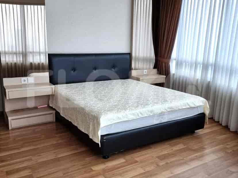 A bedroom with a queen-size bed, two bedside tables, and large windows with curtains.