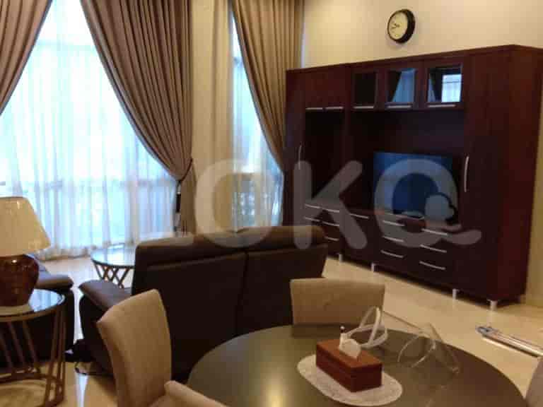Sebuah ruang tamu dengan unit hiburan kayu gelap, sofa kulit cokelat, dan meja makan bundar dengan kursi.