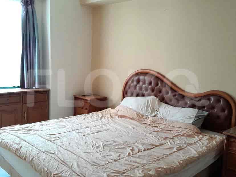 Sebuah kamar tidur dengan tempat tidur besar, nakas, dan lemari laci di dinding krem muda.