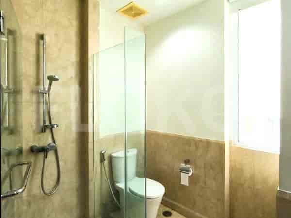 Kamar mandi dengan toilet, shower berkaca, dan dinding keramik berwarna terang.