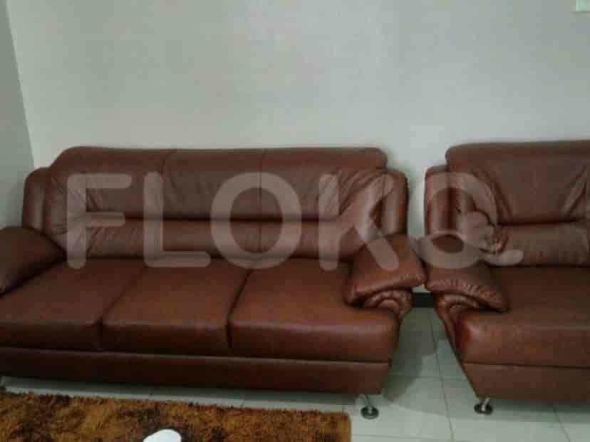 Ruang tamu modern dengan sofa kulit dan karpet sederhana.