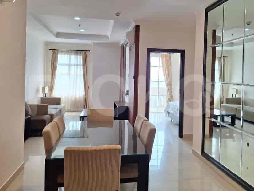Area gabungan ruang tamu dan ruang makan dengan meja makan berlapis kaca dan kursi, sofa, serta dinding cermin besar.
