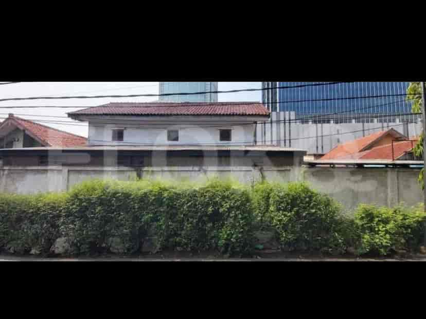 A building with a tiled roof and a long concrete fence with green shrubs in front.