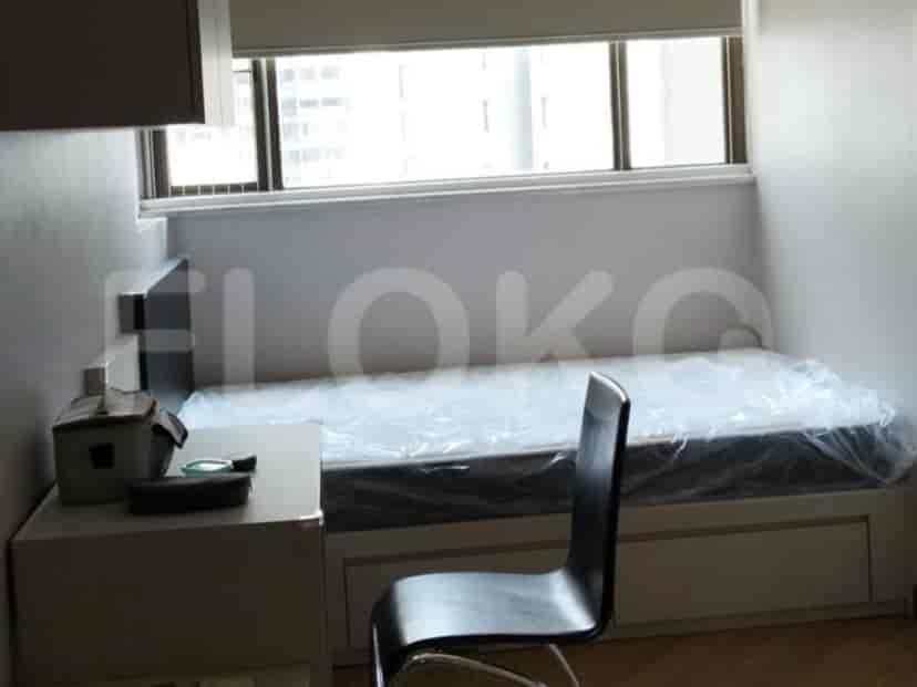 A single bed covered in plastic, a desk, and a chair in a room with a large window.