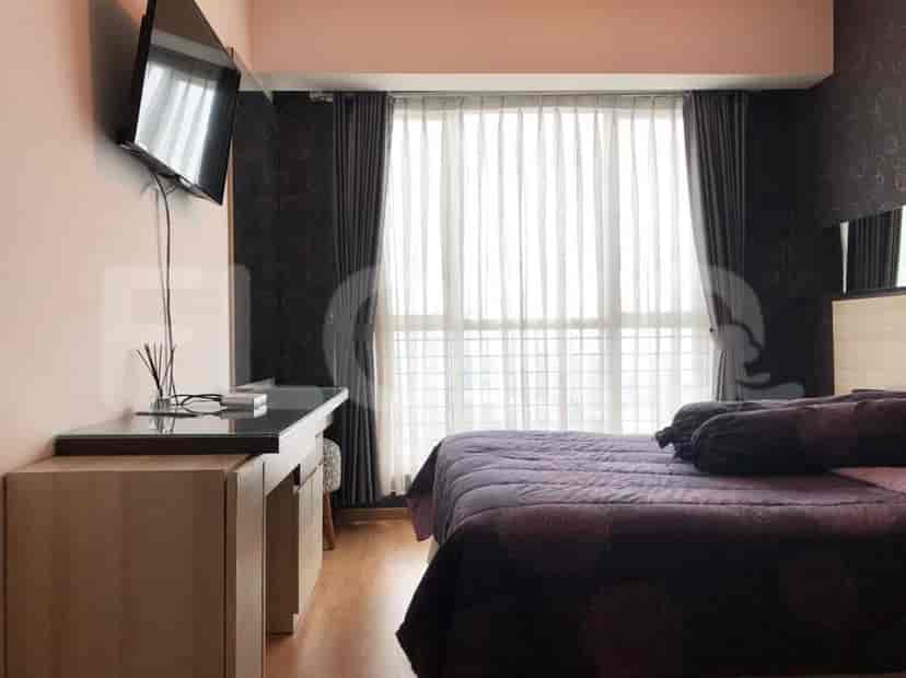 A bedroom with a queen-size bed, a TV mounted on the wall, and a desk by the window.