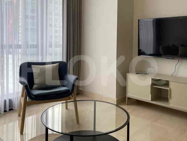 A stylish living room with an armchair, glass coffee table, and a wall-mounted TV.