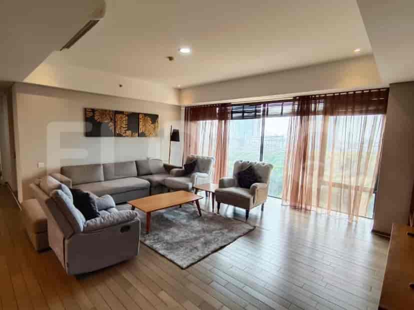 A spacious living room with an L-shaped grey sofa, two armchairs, a coffee table, and a large window with sheer curtains.