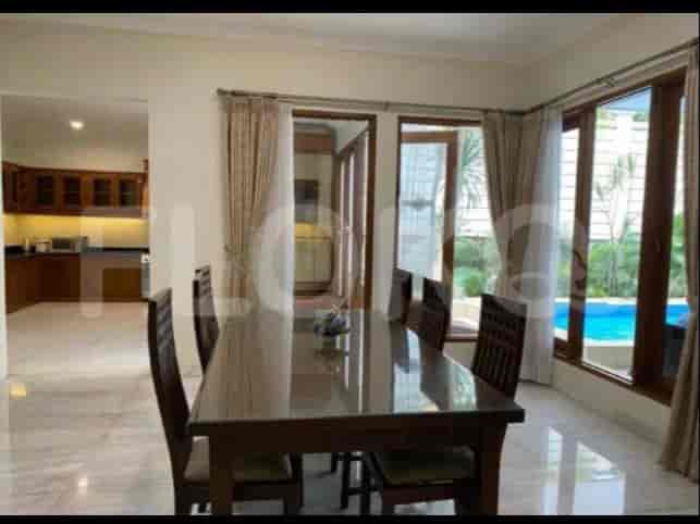 A dining area with a wooden table and chairs, overlooking a swimming pool view, with the kitchen partially visible.