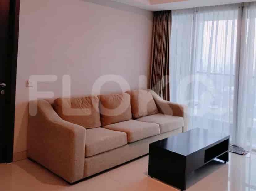 A living room with a beige sofa, a black coffee table, and large windows with curtains.