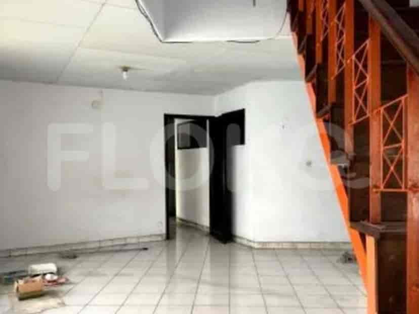 Sebuah ruangan dengan dinding putih, lantai keramik, pintu masuk gelap, dan sebagian tangga oranye.
