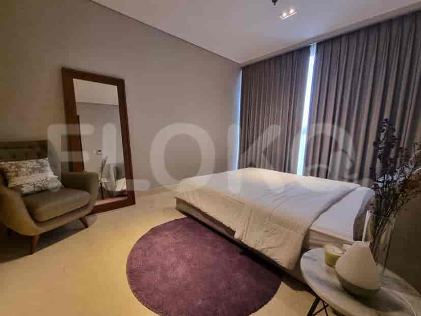 A bedroom with a bed, armchair, full-length mirror, and a small side table.