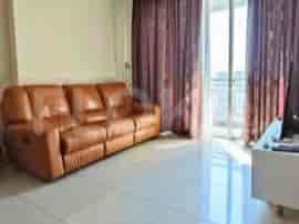 Ruang tamu dengan sofa kulit coklat, jendela besar dengan gorden ungu, dan meja TV.