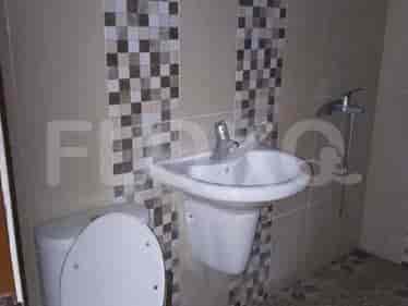 Kamar mandi kompak dengan toilet, wastafel dinding, dan dinding berkeramik.