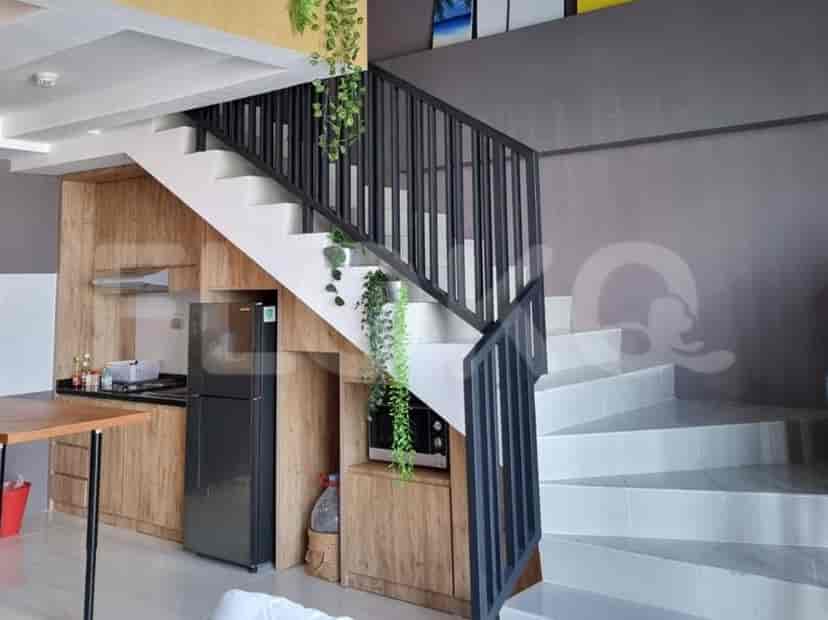 A compact kitchen area featuring wooden cabinets, a refrigerator, and microwave, adjacent to a modern staircase with black railings.