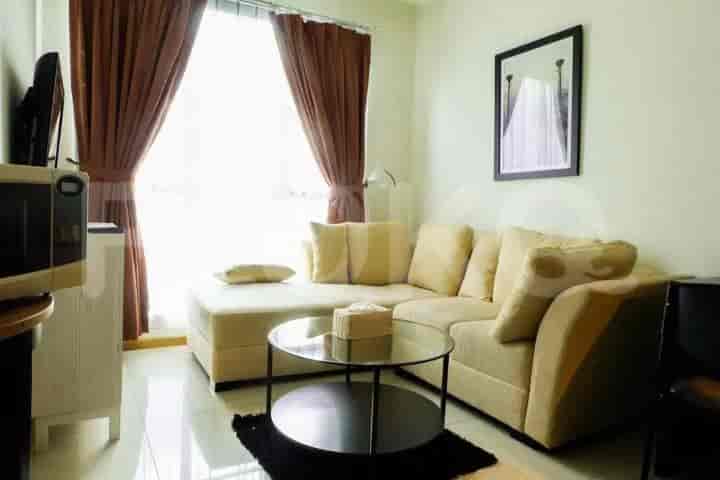 Living room with a beige sectional sofa, glass coffee table, and window with brown curtains.