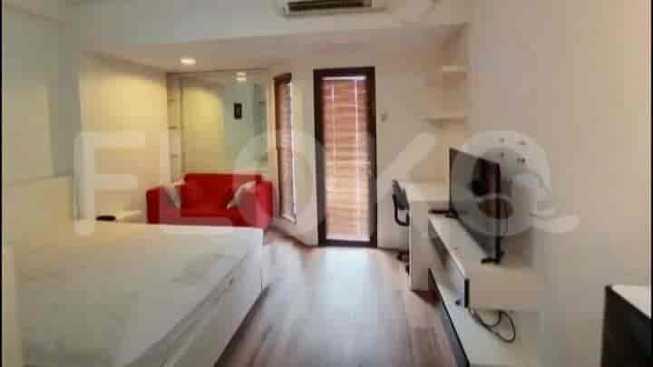 A combined living and sleeping area with a bed, sofa, and TV, featuring wooden flooring and access to a balcony.
